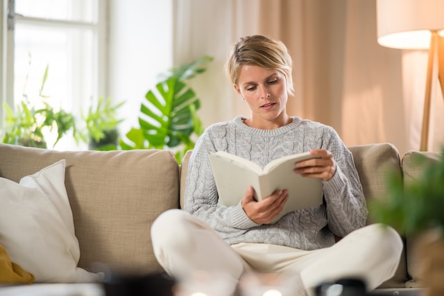 femme lisant un livre sur son canapé au lieu d'utiliser les écrans 